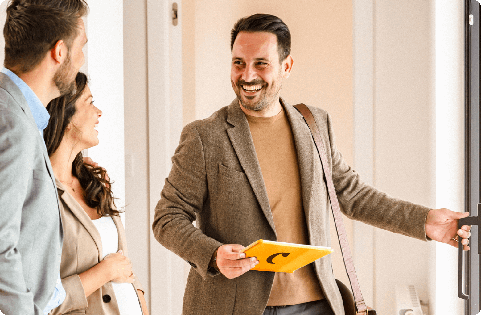 A broker holding a casavo tablet, opening the door for a couple